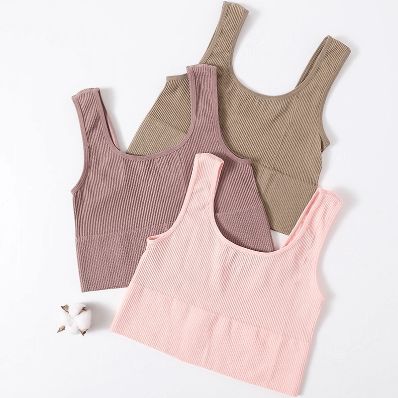 Three ribbed seamless tank tops in beige, pink, and brown for women, perfect for sports and yoga, arranged with a cotton flower.
